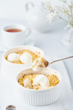 Apple crumble, spoon with ice cream, streusel. Side view, vertical. Morning breakfast on light gray table.