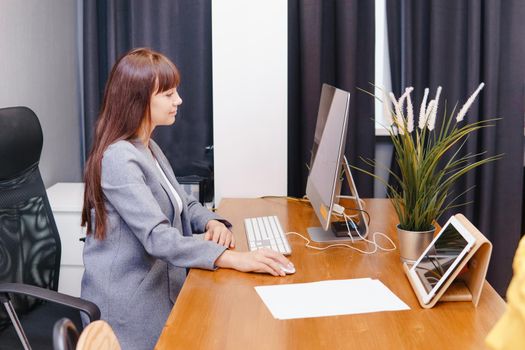A brunette woman at a computer in the workplace. Business concept.