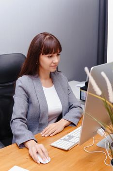 A brunette woman at a computer in the workplace. Business concept.