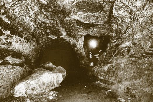 Miner man underground in a mine tunnel.  Worker in overalls, safety helmet and gummy boots is busy with work. Solarize effect