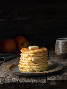 Pancake with butter. Side view, copy space, vertical. Dark moody old rustic wooden background.