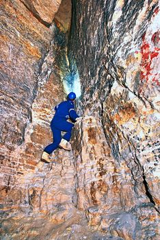 Site contractor engineer in blue overal, rubber boots and protective helmet in subterranean tunnel. The specialist checks the quality of the subsoil beneath the city.