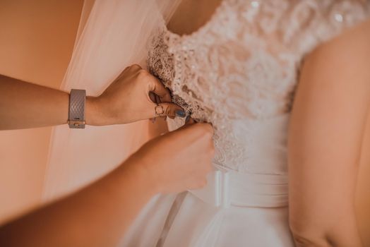 The back of the bride in a wedding dress. Mom's and woman's hands help fasten the clasps at the back.