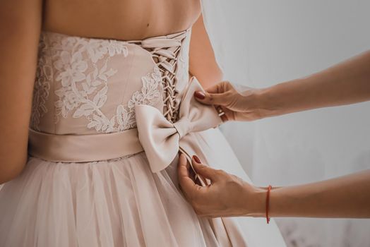 The back of the bride in a wedding dress. Mom's and woman's hands help fasten the clasps at the back.