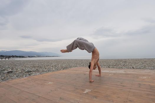 Shirtless caucasian man doing backflip on pebble beach