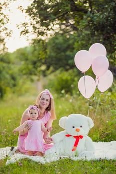 mother and daughter in pink dresses and with pink balloons in nature