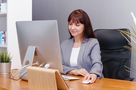 A brunette woman at a computer in the workplace. Business concept.