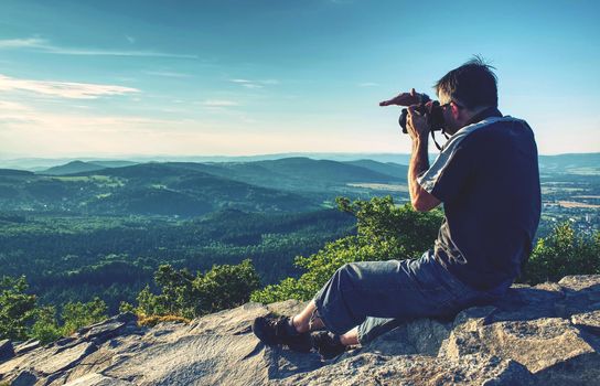 Man holding camera at eyes on mountain and watching sunset.
