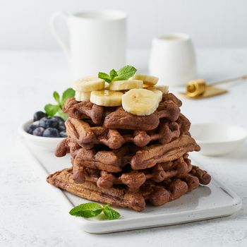 Chocolate banana waffles with maple syrup on a white table, close up, side view.