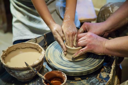 the Hands of a master and a student make a pitcher on a Potters wheel of yellow clay. Selective focus on hands