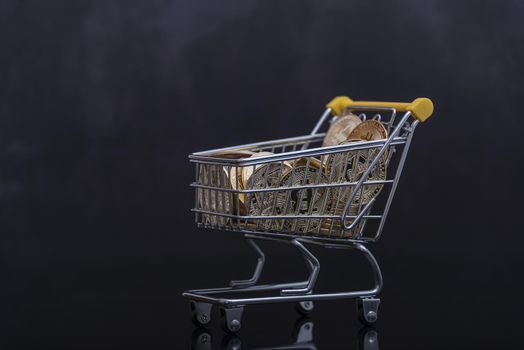 Side view of bitcoin and shopping cart on black background. Buying or selling the cryptocurrency concept. Virtual money, cryptocurrency. E-commerce concept