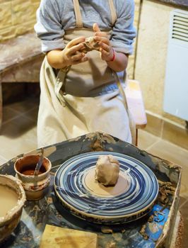 the Hands of a master and a student make a pitcher on a Potters wheel of yellow clay. Selective focus on hands