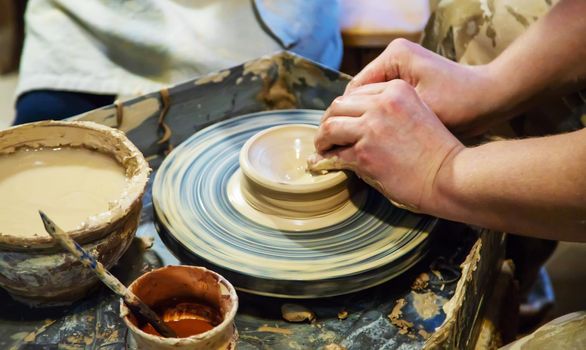 the Hands of a master and a student make a pitcher on a Potters wheel of yellow clay. Selective focus on hands