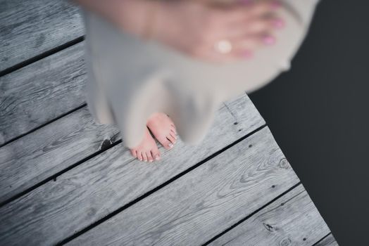 The legs of a pregnant woman in a dress are standing on a gray wooden bridge. view from above