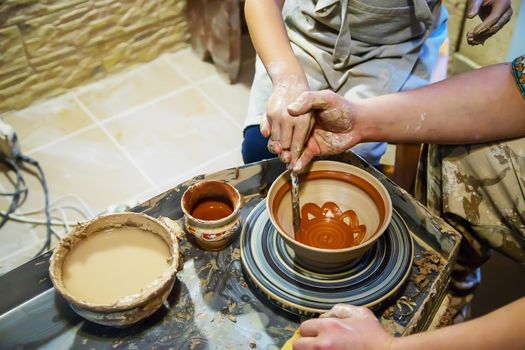 the Hands of a master and a student make a pitcher on a Potters wheel of yellow clay. Selective focus on hands