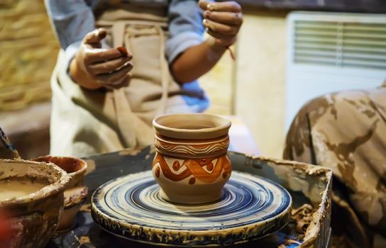 the Hands of a master and a student make a pitcher on a Potters wheel of yellow clay. Selective focus on hands