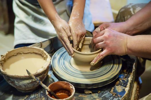 the Hands of a master and a student make a pitcher on a Potters wheel of yellow clay. Selective focus on hands