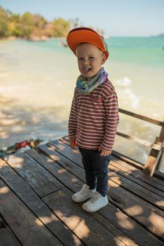 Fashion child. Happy boy model. Stylish little boy in baseball. Handsome kid. White Sneakers. red cap.Aquamarine sea background