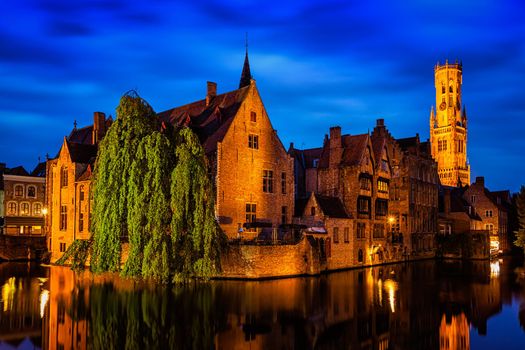 Famous view of Bruges - Rozenhoedkaai with Belfry and old houses along canal with tree in the night. Brugge, Belgium