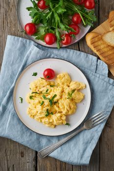 Scrambled eggs, omelette, top view, vertical. Breakfast with pan-fried eggs, cup of tea, tomatoes on the old wooden table