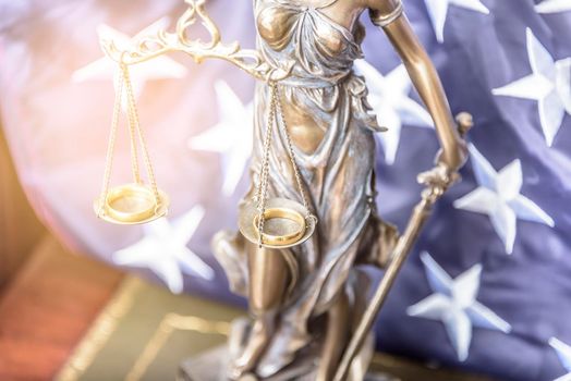 The statue of justice Themis or Iustitia, the goddess of justice blindfolded against a flag of the United States of America, as a legal concept