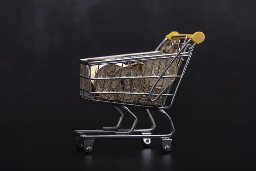 Side view of bitcoin and shopping cart on black background. Buying or selling the cryptocurrency concept. Virtual money, cryptocurrency. E-commerce concept