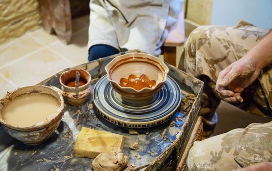 the Hands of a master and a student make a pitcher on a Potters wheel of yellow clay. Selective focus on hands