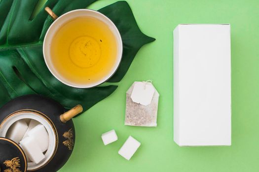 overhead view herbal tea cup with sugar cubes tea bag box green background