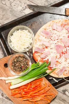 Homemade pizza on baking tray and Ingredients for cooking. From the series "Making homemade pizza"