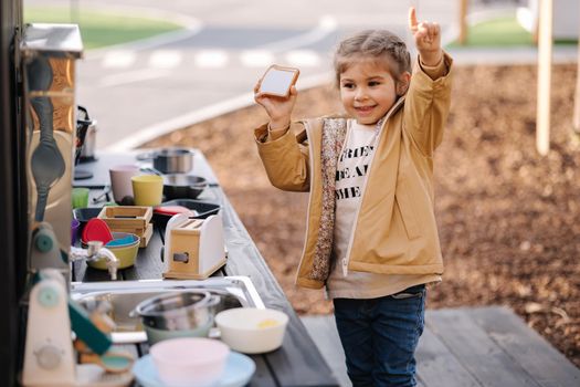 Adorable little girl playing in toy kitchen outdoors. Cute three year old girl have fun in kids city.