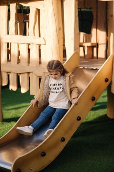 Little girl go down fron slide. Happy girl playing on playground in spring time.