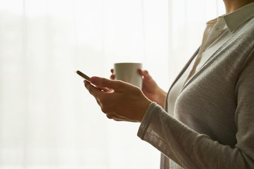 woman holding smartphone and drinking coffee/tea