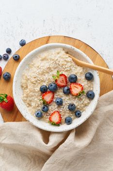 Oatmeal rustic porridge with blueberry, bilberry, blackberry, strawberry, dash diet, wooden white background top view copy space vertical