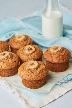 Banana muffin, side view, vertical. Cupcakes on blue napkin with milk in a bittle, white concrete table