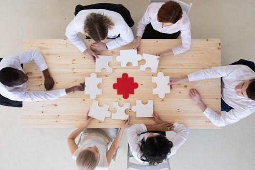 Business group assembling jigsaw puzzle at meeting table, top view