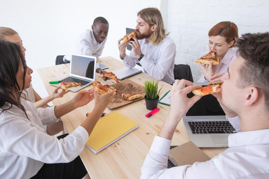Diverse business team people workers eating pizza together at workplace, friendly multi-ethnic colleagues group talking enjoying having fun and corporate lunch in office room