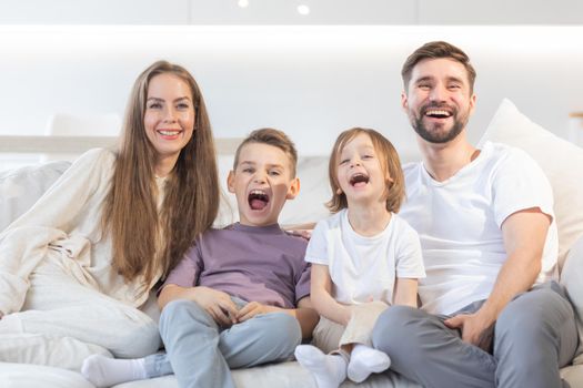 Happy family of parents with children sitting together on sofa at home