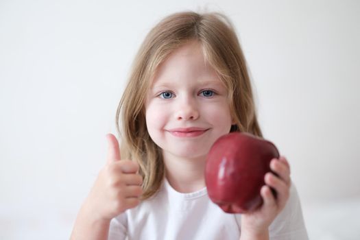 Smiling girl holding thumbs up and holding ripe apple. Benefits of fruits for children concept