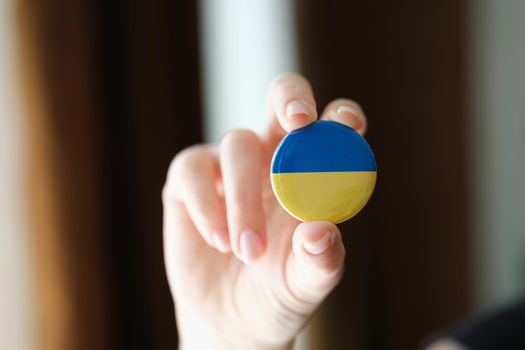 Person holds round badge Flag of Ukraine. Help and volunteering in Ukraine.