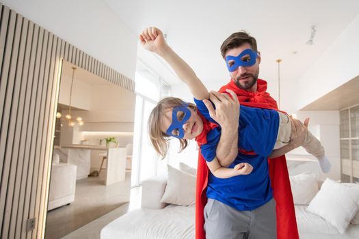 Father holding son flying in superhero costume at home