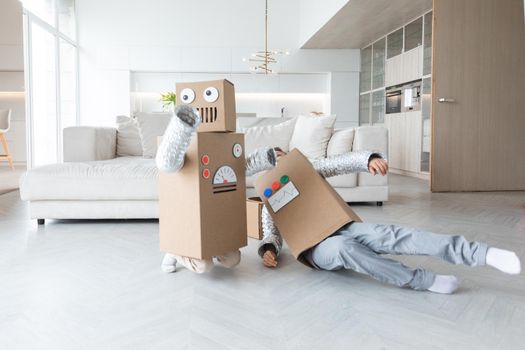 Happy two children playing robots at home, children wearing handmade moving box costume of cardboard