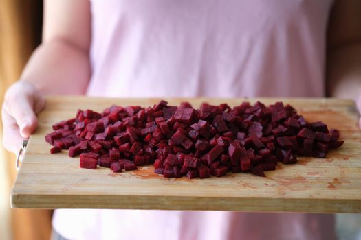 Woman is holding diced beetroot on wooden board. Cooking vegetarian food and the benefits of beetroot concept