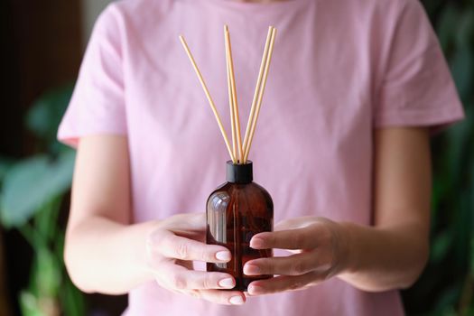 Woman holds jar with an aromatic diffuser of homemade fragrance in hands. Incense sticks and aromatherapy concept