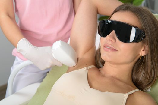 Woman receiving epilation laser treatment on armpit at beauty clinic. woman in beige lingerie