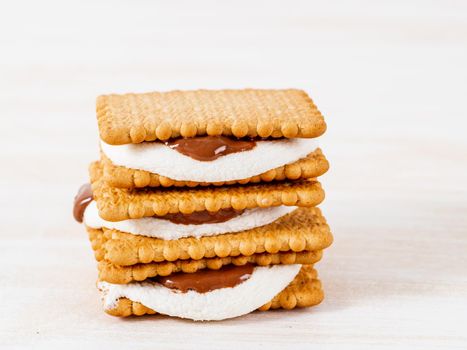 Smores, marshmallow sandwiches - traditional American sweet chocolate cookies on white wooden table, side view.