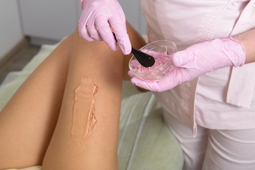 woman beautician applies contact gel on the leg of a woman for laser hair removal in medical clinic. Pink gloves