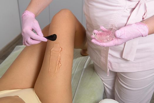 woman beautician applies contact gel on the leg of a woman for laser hair removal in medical clinic. Pink gloves