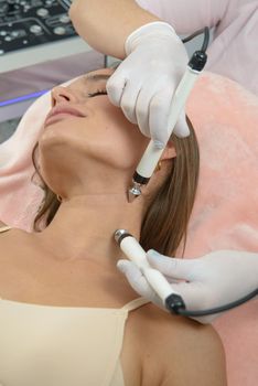 Cosmetology. Beautiful woman at spa clinic receiving stimulating electric facial treatment from therapist. Closeup of young female face during microcurrent therapy. Beauty treatment. High resolution