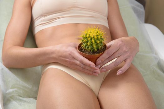 Depilation in the bikini zone concept. A woman holding a yellow cactus in her hand laying in light beige pants.