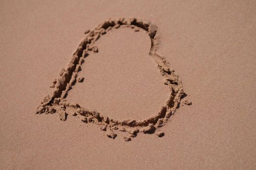 Seashore with sand and hearts. Ocean coast and beach coast. Drawing of a heart on sandy beach with sunlight.